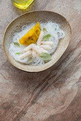 Bowl of soy bean noodles with tteokbokki and steamed dumpling on a brown stone background, vertical shot with space, top view