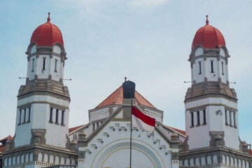 Detailed view of the Lawang Sewu building with the red and white flag and a bright blue sky in the background