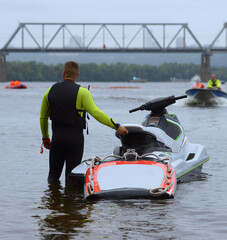 Naklejka premium Man rescuer standing in the water by scooter waiting for motorboat approaching, bridge on a background, autumn