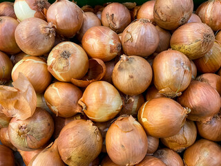 A close up, high angle view of a large pile of whole raw yellow onions with golden brown papery skins, gathered together in a bin or crate for sale at a market or grocery store