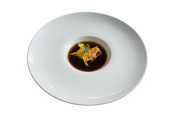 Elegant culinary presentation of a dark broth with garnish on a white plate