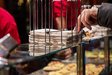 Customer reaching for a white napkin from a metal holder while vendors work behind the counter at a...