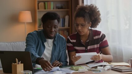 Waist up of young adult Biracial couple sitting at home using laptop and reviewing bills, calculating expenses and managing household finances or budgeting together - Powered by Adobe