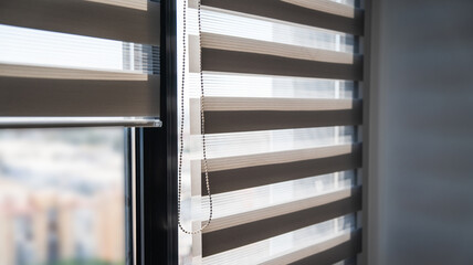 Striped zebra blinds on sunlit window creating alternating translucent and opaque layers in modern interior © Volodymyr_sh