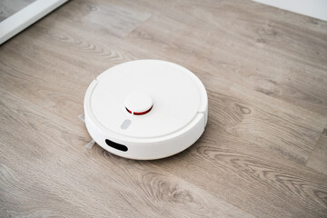 White robotic vacuum positioned on wood flooring while cleaning open interior zone in bright modern...