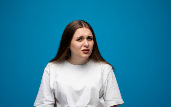 Young woman with confused and skeptical facial expression posing against blue background in studio.