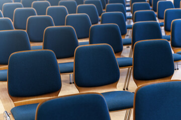 Fototapeta premium Rows of blue chairs stand in empty hall creating calm geometric pattern. Soft fabric surfaces reflect gentle light forming orderly rhythm and inviting atmosphere