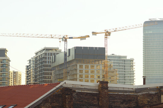Landscape with an old building, a modern residential complex and working tower cranes, taken in the golden hour. Represents neighborhood transformation, contrasts, urban planning, and city evolution.