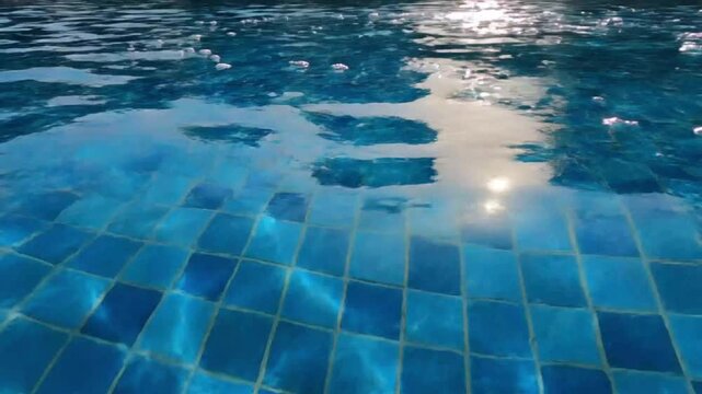 Swimming pool water surface with sunlight reflection and blue tile floor