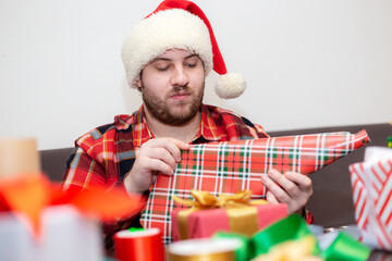A young, bearded Caucasian man wearing a plaid shirt wraps Christmas presents.