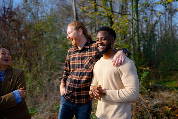 Group of friends laughing together in a park during a sunny afternoon in fall with trees in background