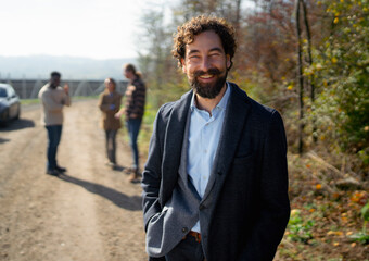 Smiling man stands on a dirt road with friends in a nature setting during sunny weather