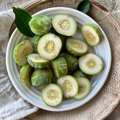 A closeup overhead view of several green, unripe or wild kiwi fruit, some whole and some halved, arranged on a white plate