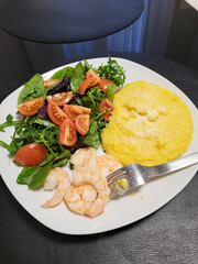 Healthy plate with shrimp, creamy polenta and fresh salad. Balanced homemade meal with cherry tomatoes, greens and cooked seafood.