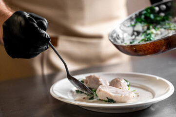 Chef plating a gourmet dish of chicken with creamy sauce and spinach in a professional kitchen setting.