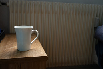 White china cup on a bedside table with soft backlight in a simple real-life home setting. Natural unpolished everyday moment. Concept of morning, home, routine, simplicity.
