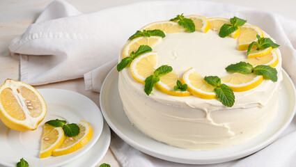 Delicious lemon cake with white frosting decorated with lemon slices and fresh mint leaves on a plate. Fresh, bright and appetizing dessert.