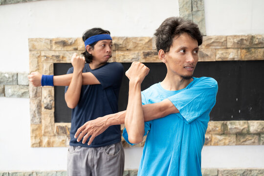 Two southeast asian men are stretching their arms and one of them is wearing a blue shirt