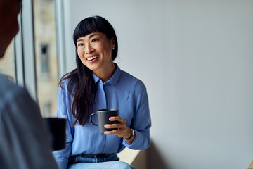 Asian Woman In Blue Shirt Smiling With Coffee Mug By Window In Modern Office