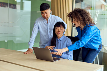 Asian Woman Leads Collaborative Office Meeting With Colleagues Around Laptop During Teamwork Session In Modern Workspace