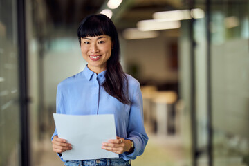 Asian Business Woman In Blue Shirt Holding Paper In Modern Office Hallway