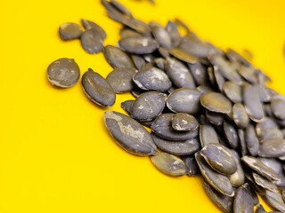 Dried pile of pumpkin seeds against a yellow background