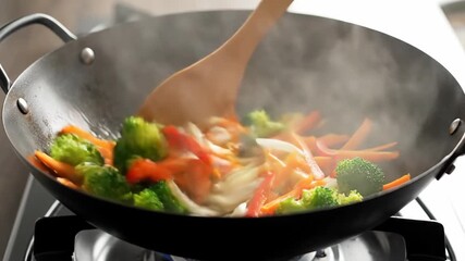 A wok is filled with colorful vegetables, steam rising as they cook. A wooden utensil is stirring the mix - Powered by Adobe
