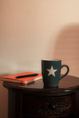 Grey mug with orange notebook and a pen resting on wooden table.