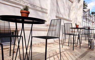 Outdoor café tables with black metal chairs and small potted plants representing relaxed social spaces and urban leisure in a peaceful neighborhood