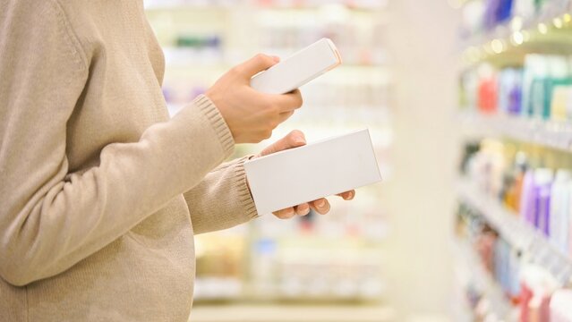 Woman reading and examines ingredient labels while comparing and choosing between cosmetic products, cream and serum, in a beauty store aisle, focusing on making an informed decision.