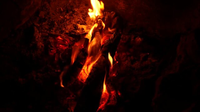 Close-up campfire with burning sticks in darkness, showing glowing embers and flickering flames, perfect for camping, survival visuals, warm firelight and flame motion, adventure, cozy fire concepts