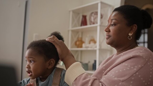 Adorable African American toddler girl babbling while her loving mother brushing her hair