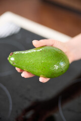 A large avocado in a woman's hand in the interiors of a bright and spacious kitchen