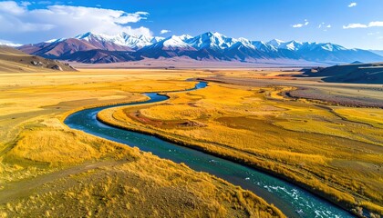Serpentine river flows through a golden grassland toward snow-capped mountains under a vibrant blue sky