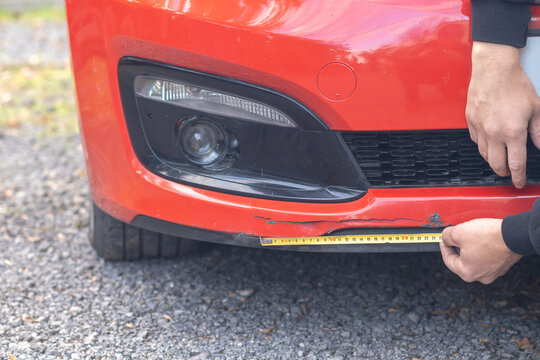 A man measures the length of a crack in his car after an accident.