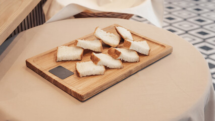 Sliced bread on a wooden board. Irregularly cut pieces of white bread on a small, light wooden serving board. 