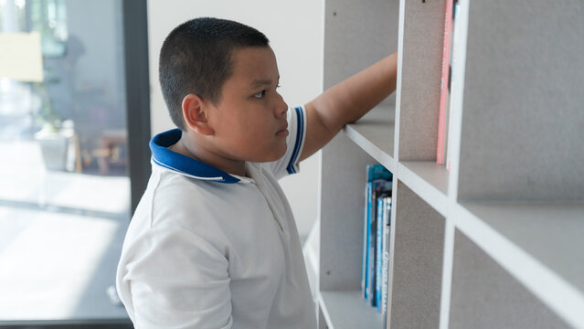 Young boy browsing a bookshelf, searching for a book to read at home or school - Powered by Adobe