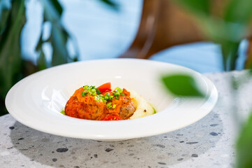 A close-up shot of a gourmet dish featuring meatballs served over creamy mashed potatoes, topped with rich tomato sauce and fresh green onions on a white plate