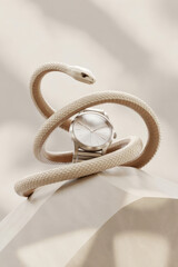 Watch with a fake snake wrapped around it, creating striking visual contrast and highlighting bold fashion accessory styling in a dramatic still life setup.