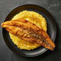 A perfectly panfried, crispy catfish fillet served atop a bed of creamy, bright yellow grits on a dark plate