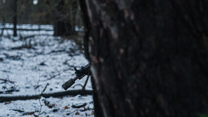 Soldier on a military mission in the wilderness. Forest at winter. Aiming from behind a tree. War tactics