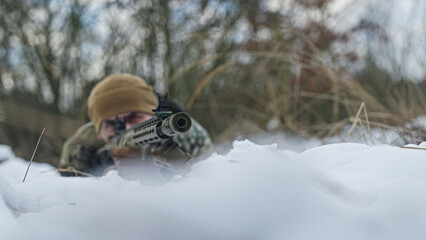 Soldier on a military recon mission. Forest at winter. Hiding in the heaps of snow and aiming. War tactics. Tactical Extension Choke.