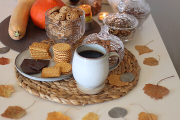 Lit candles, cookies, chocolate, nuts, tea, wine, pumpkins, books, reading glasses and autumn leaves on the table. Autumnal hygge at home. Selective focus.