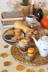 Lit candles, cookies, chocolate, nuts, tea, wine, pumpkins, books, reading glasses and autumn leaves on the table. Autumnal hygge at home. Selective focus.