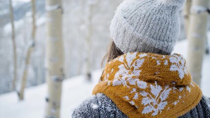 Video A woman stands in a snowy landscape wearing a hat and scarf, perfect for winter scenes or cold weather inspiration