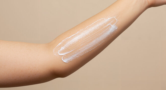Arm applying lotion on smooth skin against a neutral background  