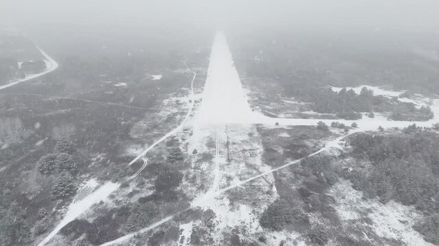Slow motion approaching and circling the edge of the snowy, empty runway at the decommissioned Killaloe / Bonnechere Airport in Ontario, Canada, during heavy winter snowfall