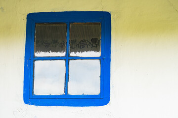Gray and gray-washed wall with blue framed window 3 small left, 1 large right, reflecting unseen...