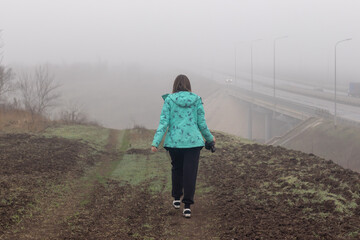 A young woman in a coat walking outside the city on a foggy autumn morning