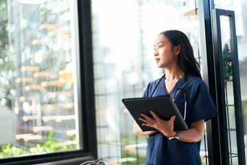 Asian female doctor or nurse holding tablet looking out window